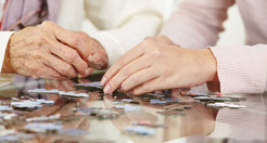 on the left you see the hand of an older person, on the right the hand of a younger person, both are doing a puzzle